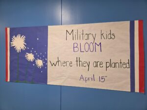 A student-made banner hung in a hallway that reads Military kids BLOOM where they are planted April 15th