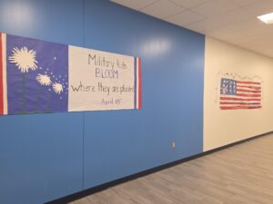 Angle view of a student-made banner hung in a hallway that reads Military kids BLOOM where they are planted April 15th